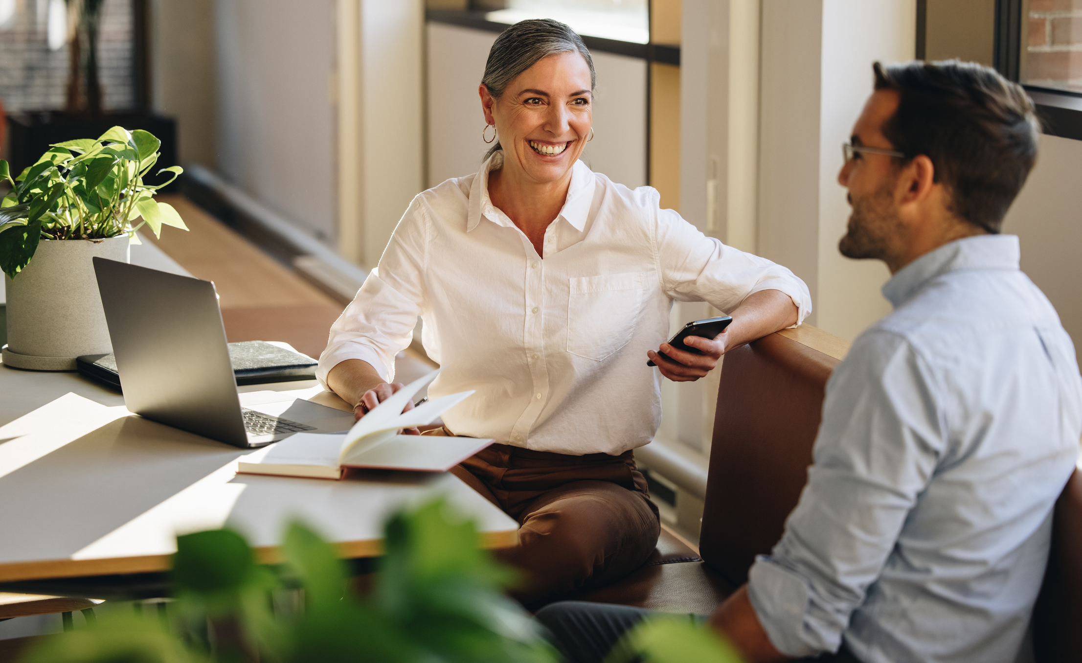 A man and woman in a modern office collaborating with a laptop and notepad